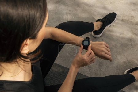 Foto de Tired slender caucasian millennial female in sportswear sits on mat, checks pulse after activity workout on street, cropped. Sports, fitness, active in city, cardio training, body care and slimming - Imagen libre de derechos