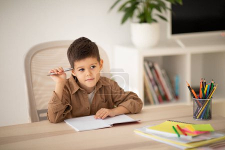 Photo for Serious pensive cute european small kid thinking, drawing, study at table in living room, elementary school, kindergarten interior. Art, modern education for children at home, creating idea for lesson - Royalty Free Image