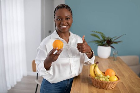 Photo for Friendly pretty young african american woman in smart casual outfit dietitian recommending fresh juicy orange, showing thumb up and smiling at camera, diet, detox, vitamins and minerals, copy space - Royalty Free Image