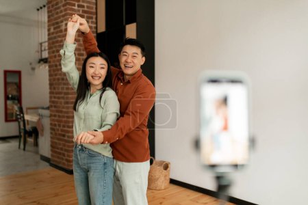 Téléchargez les photos : Joyeux couple asiatique diffusant tout en dansant et s'amusant ensemble à la maison, vloggers enregistrement vidéo en face de la caméra smartphone, copier l'espace - en image libre de droit