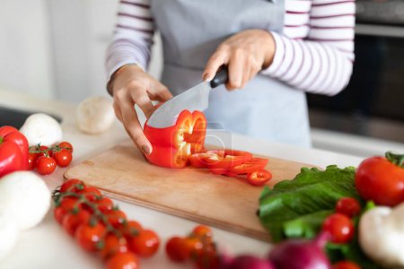Photo for Female hands cutting fresh organic red bell pepper, unrecognizable woman wearing apron housewife preparing healthy meal, chopping fresh vegetables, kitchen interior, cropped - Royalty Free Image