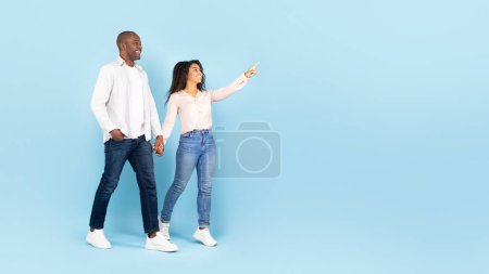 Photo for Happy african american spouses walking and holding hands, woman pointing finger at free space, blue background, panorama. Great ad and offer, romance, love and relationship - Royalty Free Image