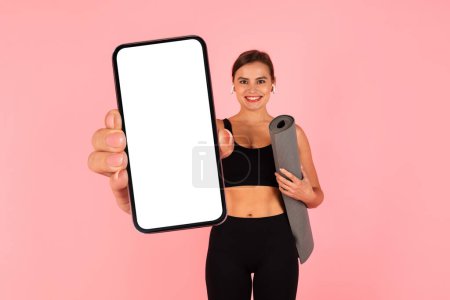 Téléchargez les photos : Online Offer. Sporty Young Lady With Yoga Mat Showing Big Blank Smartphone With White Screen At Camera, Athletic Woman Recommending Fitness Application, Standing Over Pink Background, Collage, Mockup - en image libre de droit
