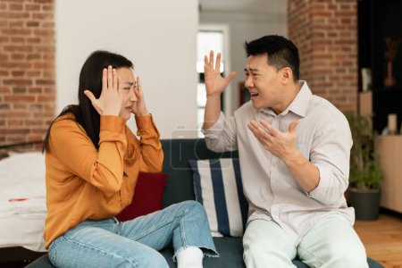 Photo for Marital problems, divorce concept. Married japanese couple having fight, yelling at each other, sitting on sofa in living room. Furious man and woman shouting at one another - Royalty Free Image