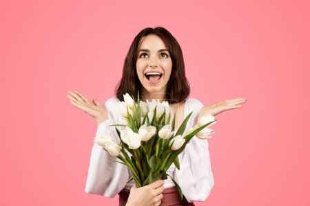 Téléchargez les photos : Happy excited young european lady with open mouth rejoices to gift bouquet of flowers, enjoys lifestyle, spring holiday, isolated on pink background, studio. Date, surprise, beauty care, ad and offer - en image libre de droit