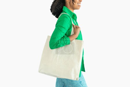 Téléchargez les photos : Unrecognizable Black Woman Carrying Textile Shopper Bag Posing On White Background In Studio. Cropped Shot Of Modern Customer Lady. No More Plastic Concept. Cropped, Side View - en image libre de droit