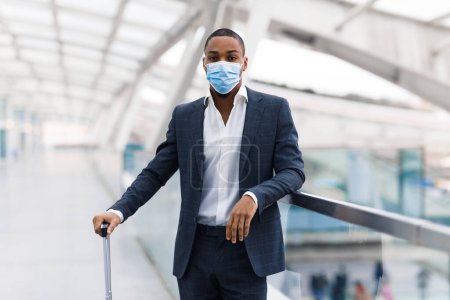 Téléchargez les photos : Portrait Of Young Black Businessman Wearing Medical Mask Standing At Modern Airport, African American Male In Suit Waiting For Flight At Terminal, Travelling During Coronavirus Pandemic, Copy Space - en image libre de droit