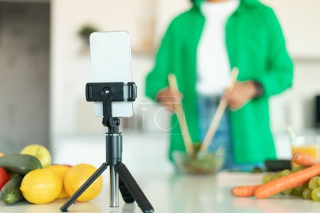 Photo for Cropped Shot Of Food Blogger Woman Filming Video On Smartphone And Making Healthy Vegetable Salad Standing In Modern Kitchen At Home. Cooking Blog Concept. Selective Focus On Mobile Phone - Royalty Free Image