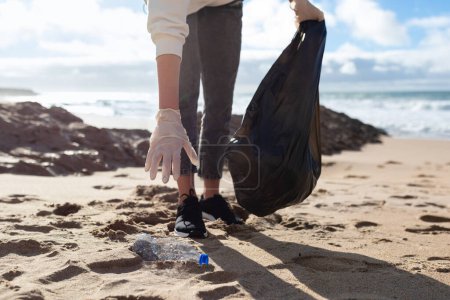 Foto de Mujer joven recogiendo basura de plástico de la playa y ponerlo en la bolsa de plástico para reciclar, disparo de primer plano. Limpieza y reciclaje, Save earth concept - Imagen libre de derechos
