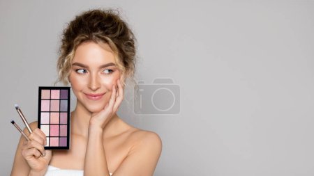 Photo for Beautiful young woman with eye shadow makeup palette posing over grey background, looking aside at free space, banner. Lady with healthy perfect skin. Cosmetology, beauty and spa - Royalty Free Image