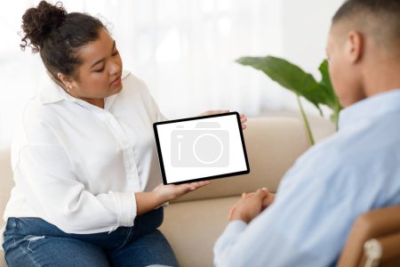 Téléchargez les photos : Online therapy app, modern technologies in psychotherapy concept. Mixed race plus size woman therapist showing male patient black guy digital tablet with blank screen during session, mockup - en image libre de droit