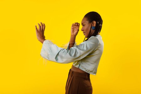 Photo for Pretty Black Female Pretending Holding Telescope In Hands Or Watching Through Spyglass Looking Aside Standing Over Yellow Studio Background. Let Me See Concept. Side View Shot - Royalty Free Image
