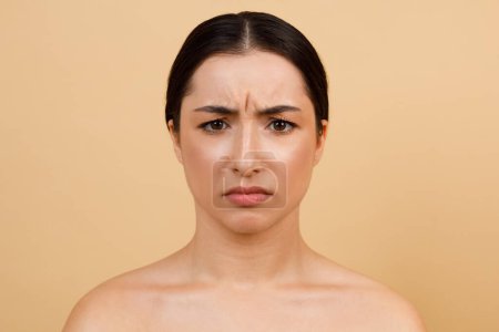 Glabellar Lines. Portrait Of Unhappy Young Indian Woman Frowning While Looking At Camera, Beautiful Hindu Female With Brow Furrow Standing Isolated Over Beige Studio Background, Copy Space