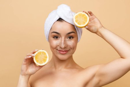 Photo for Skincare Concept. Beautiful Young Indian Woman With Towel on Head Holding Lemon Halves, Attractive Hindu Female Using Organic Antioxidant Fruit For Beauty Routine, Standing On Beige Background - Royalty Free Image