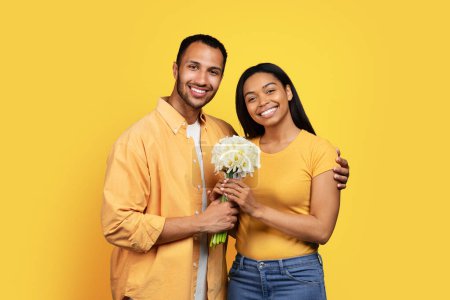 Photo for Cheerful young black male giving bouquet of flowers to woman hugging, enjoy relationships, isolated on yellow background, studio. Romance, love and date, congratulations on holiday, Valentine day - Royalty Free Image