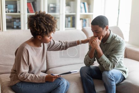 Photo for Friendly beautiful african american woman psychologist consoling upset young man, black female psychologist touching sad crying guy patient shoulder, clinic interior. Psychological support concept - Royalty Free Image