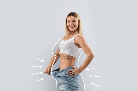 Photo for Happy positive middle aged pretty blonde lady wearing big jeans, showing loose in waist and smiling at camera, grey studio background, side view, copy space, collage - Royalty Free Image