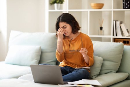 Foto de Young Arab Woman Feeling Tired After Working Online On Laptop At Home, Exhausted Middle Eastern Female Student Taking Off Glasses And Rubbing Nosebridge, Suffering Headache, Copy Space - Imagen libre de derechos