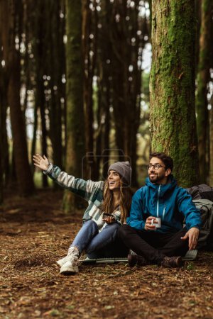 Photo for Happy millennial caucasian family in jackets with backpack travel, show hand to cold forest, enjoy adventure together outdoor. Sports at weekend, vacation, active lifestyle and camping, hikers at walk - Royalty Free Image