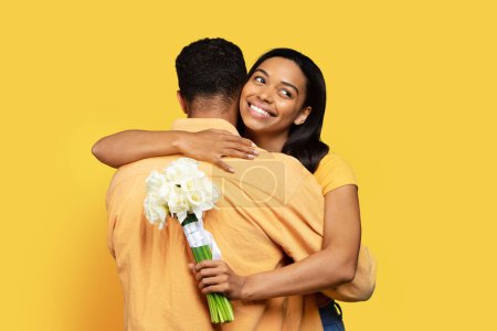Photo for Happy young african american male giving bouquet of flowers to wife, hug isolated on yellow background, studio. Celebrate anniversary, Valentine day, romance, love and date, congratulations on holiday - Royalty Free Image