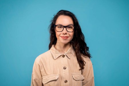 Téléchargez les photos : Portrait of glad pretty smart millennial european female student in glasses looking at camera, isolated on blue background, studio, empty space. Lifestyle, study, work, ad and offer, facial expression - en image libre de droit