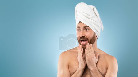 Téléchargez les photos : Portrait d'homme torse nu et drôle avec serviette sur la tête regardant dans l'excitation de côté à l'espace libre, posant sur fond bleu studio, panorama. - en image libre de droit