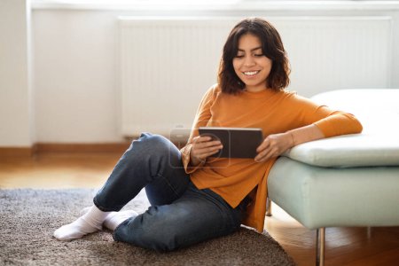 Photo for Technologies For Leisure. Beautiful Middle Eastern Female Using Digital Tablet At Home, Happy Arab Woman Browsing Social Media Or Shopping Online On Modern Gadget, Resting On Floor In Living Room - Royalty Free Image