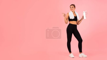 Photo for Fitness Offer. Young Athletic Female In Sportswear Pointing Aside At Copy Space While Standing Over Pink Studio Background, Sporty Woman With Water Bottle In Hands Showing Free Place For Ad, Panorama - Royalty Free Image