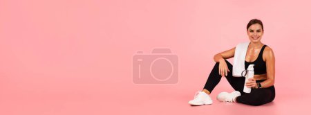 Photo for Fitness Concept. Happy athletic lady sitting on the floor with water bottle in hand and looking at camera, smiling young sporty woman relaxing after training, posing over pink background, copy space - Royalty Free Image
