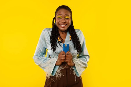 Téléchargez les photos : Thrilled African American Woman Holding Carte de crédit debout sur fond jaune Studio. Femme Client Posant Publicité Great Bank Offre sourire à la caméra. Finances Sécurité - en image libre de droit