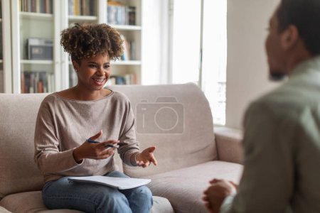 Photo for Smiling cheerful pretty stylish young black woman therapist chatting with man patient, providing professional psychological help, giving useful tools and techniques to avoid depression, copy space - Royalty Free Image