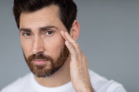 Téléchargez les photos : Anti-aging eye care treatment. Handsome middle aged man touching under eyes skin and looking at camera, closeup, grey studio background, copy space - en image libre de droit