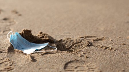 Foto de Mascarilla quirúrgica usada tirada en la orilla del mar de playa, residuos médicos, basura, basura en agua de mar, panorama con espacio libre. Coronavirus contaminación enfermedad el medio ambiente - Imagen libre de derechos