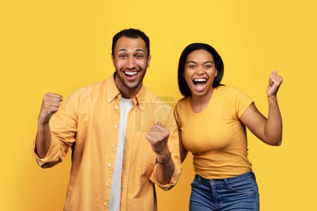 Téléchargez les photos : Glad excited young african american couple shouting, have fun, make success sign with hand in free time, rejoice in victory isolated on yellow background, studio. Relationship, emotions, ad and offer - en image libre de droit