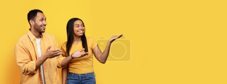 Photo for Smiling young african american man and female show hands on empty space, isolated on yellow background, studio, panorama. Relationship and love, recommendation and advice sale, news, ad and offer - Royalty Free Image
