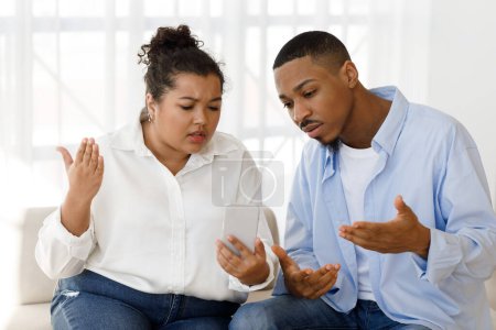 Emocional pareja joven de raza mixta tienen reunión en línea con el terapeuta familiar, el hombre negro y la señora hispana gordita sentado en el sofá en casa, utilizando el teléfono celular, haciendo gestos mientras que la videollamada con el psicólogo