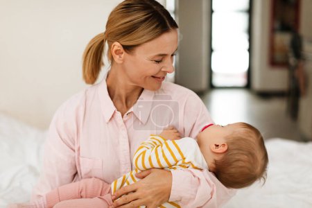 Photo for Mothers care. Mom holding her sleeping baby daughter on hands, sitting on bed at home, caring for her infant girl while she sleeping peacefully - Royalty Free Image