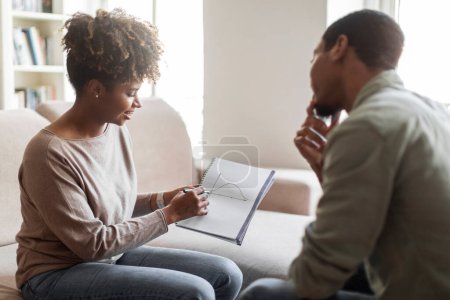 Photo for Attractive african american young woman psychologist having conversation with male patient, showing him charts, explaining mental processes. Black guy attending therapy session, copy space - Royalty Free Image
