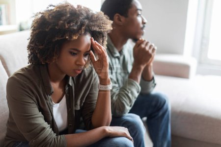 Unzufriedene schwarze Millennials in lässigen Outfits sitzen zu Hause auf dem Sofa, Mann und Frau fühlen sich nach Streit niedergeschlagen, Ehepartner denken über Scheidung nach, brauchen Familientherapie, Kopierraum