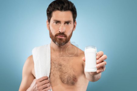 Photo for Personal hygiene and treatment after shower. Middle aged shirtless man with towel showing deodorant for armpit, posing over blue studio background, selective focus, mockup - Royalty Free Image