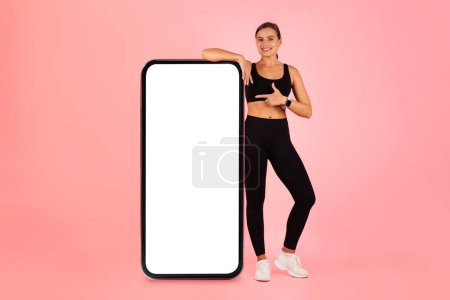 Photo for Mobile Mockup. Smiling Sporty Lady Pointing At Big Blank Smartphone Screen, Happy Slim Female In Sportswear Indicating Copy Space For Fitness Ad, Standing On Pink Background, Collage, Mockup - Royalty Free Image