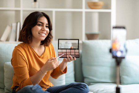 Photo for Smiling Young Arab Woman Making Makeup Video Tutorial While Sitting In Front Of Camera At Home, Happy Middle Eastern Female Blogger Demonstrating Eyeshadow Palette, Advertising New Cosmetics - Royalty Free Image