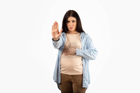 Téléchargez les photos : Strict young pregnant lady gesturing stop looking severely at camera forbidding or warning, standing isolated over white studio background, copy space - en image libre de droit