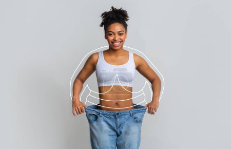Photo for Happy young slim african american woman in big jeans enjoying weight loss result with abstract lines around body, isolated on gray wall background, studio. Health and body care, diet, fit and sport - Royalty Free Image
