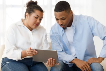 Photo for Attractive young plump hispanic woman psychologist having conversation with male patient, showing him digital pad, explaining mental processes. Depressed black guy attending therapy session - Royalty Free Image