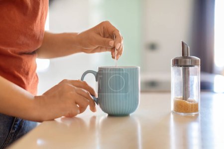 Téléchargez les photos : Closeup Shot Of Unrecognizable Woman Preparing Coffee In Kitchen, Young Female Holding Tea Spoon And Stirring Brown Sugar In Cup While Making Caffeine Drink In The Morning, Side View - en image libre de droit