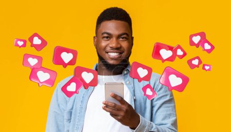 Foto de Glad black adult man with beard has romantic chat with hearts on smartphone enjoys message, social networks on orange studio background, close up, panorama. App for dating remotely, relationships - Imagen libre de derechos