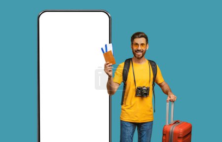 Téléchargez les photos : Happy middle aged man holding passport and tickets, standing with suitcase and backpack next to big phone with mockup on blue background, studio shot. Travel, vacation, online mobile app, collage - en image libre de droit