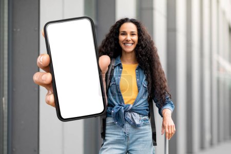 Foto de Happy Female Tourist Standing In Airport And Showing Big Blank Smartphone, Smiling Beautiful Traveller Woman Recommending Mobile Application For Booking Tickets Online, Collage, Mockup - Imagen libre de derechos
