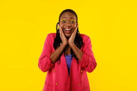 Téléchargez les photos : Excited African American Woman Touching Face Looking At Camera In Excitement Posing Over Yellow Background, Wearing Bright Pink Jacket. Wow Offer Concept. Studio Shot - en image libre de droit